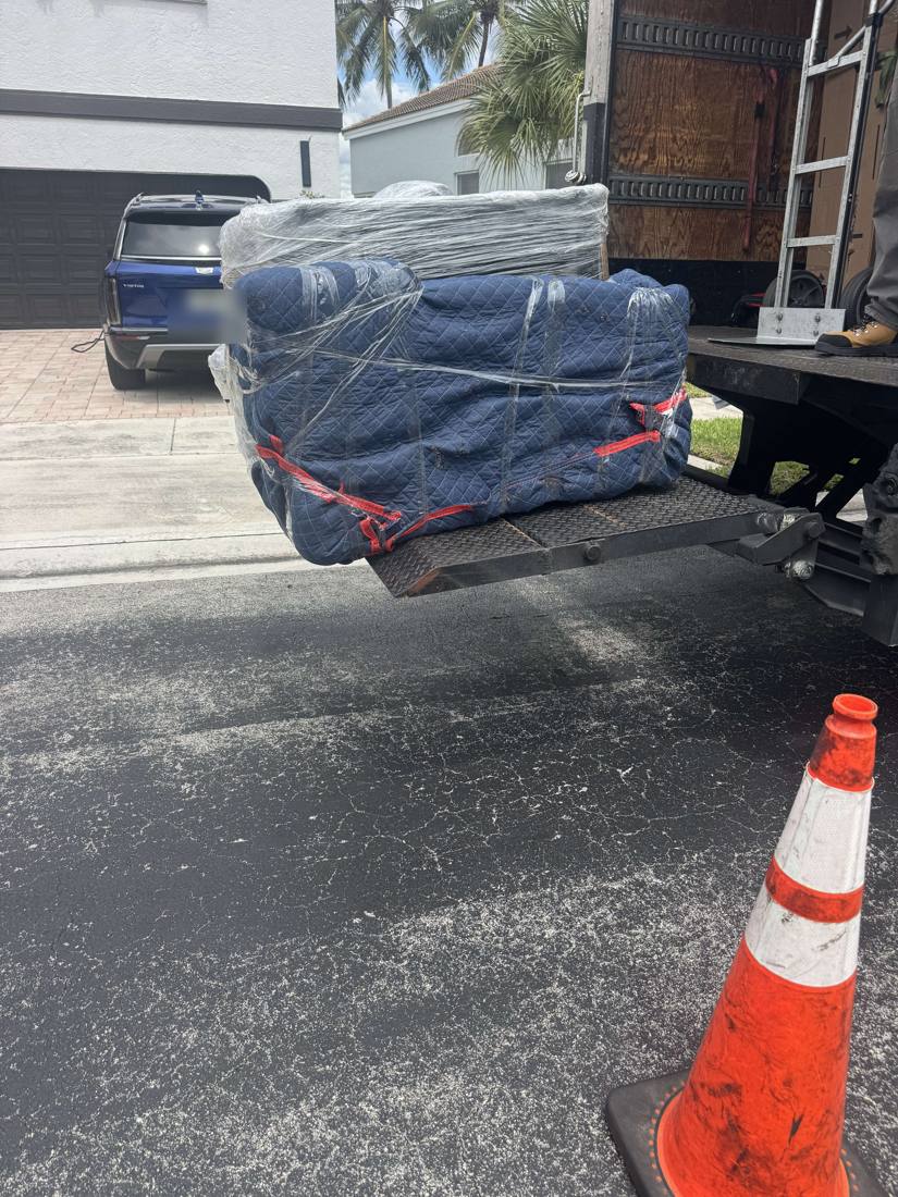 Sofa wrapped in moving blankets and plastic on a truck liftgate